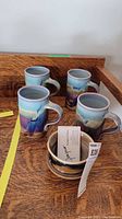 Overview image of four mugs and one bowl with Gagnier Ross pottery glaze on a wooden surface.
