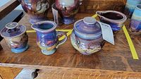 Four pieces of Gagnier Ross pottery displayed on wooden surface including a covered jar, pitcher, and two small pots.