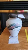 Full view of Allan Pace pottery vase on wooden surface with identification tag attached.