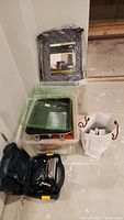 Clear plastic storage bins with painting supplies, rollers, trays, and a gray quilted China storage bag packaged and placed on floor