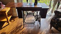 Full view of vintage Singer sewing machine mounted in wooden table with treadle base, showing left side and drawer details.