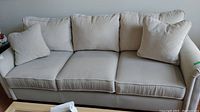 Front view of the beige Lazy Boy 3-seat sofa with three seat and three back cushions plus two throw pillows.