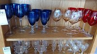Shelf of assorted colored stemware including blue, amber, red, and clear glasses arranged in rows