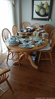 Full view of the pine oval dining table with assorted dishes on top and 8 matching chairs around it in a dining room.