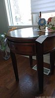 Full view of round wooden side table showing single drawer and tapered legs