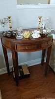 Wood hall table with semi-circular inlay top and single drawer, shown from front, complete with various glass decorative items on top (not included)