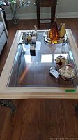 Top view of coffee table showing clear beveled glass insert surrounded by light wood frame with items on tabletop.