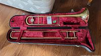 Full view of trombone in open hard case with red velvet interior and no mouthpiece present.