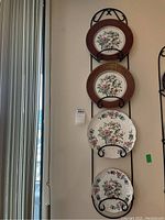 Four Aynsley decorative plates mounted vertically on black metal plate wall hanger against wall.