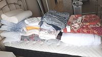 Full display of assorted bed linens, pillows, and blankets arranged on double mattress