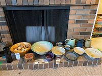 Overview photo of the lot showing ceramic bowls and pitchers on a fireplace hearth, a wooden bowl with natural decorative items, and some cards.