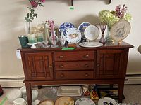 Wooden buffet table topped with decorative items such as plates, vases, candles, and flowers.