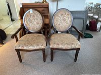 Front view of two matching wooden armchairs with upholstered seats and backs, positioned side by side on carpet.