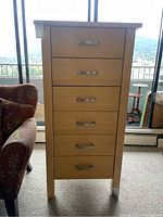 Front view of tall wooden chest of drawers with six drawers and metal handles. Shows wear and metal caps on legs.