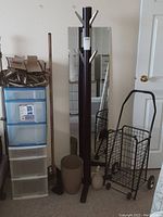 Photo of the lot showing coat rack, mirror, broom, watering can, wastebasket, shopper cart, and storage chests