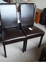 Two matching dark brown cushioned chairs with faux leather upholstery, showing wear and damage on seat covers.