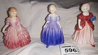Photo of three porcelain figurines: Rose in pink dress, Marie in purple dress, Miss Pamela in red and pink dress holding a blue book.