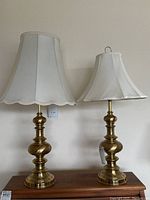 Pair of two matching brass lamps with different fabric shades placed side by side on a wooden surface.