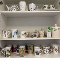 Three shelf display of assorted ceramic mugs, cups, teapots, and tea canister with various floral and seasonal designs