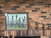 Overall view of framed painting and three wood carved owls against brick backdrop