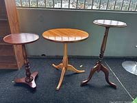 Three wood side tables with different finishes and designs photographed indoors on carpet against wall