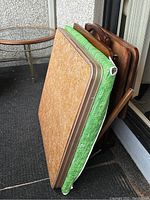 Side view of two card tables with beige laminated tops and green patterned edges, and three wooden TV trays with handles.