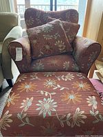 Front view of the floral upholstered armchair with a matching ottoman and two throw cushions.