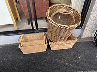 Six wicker baskets including a large round basket and multiple rectangular baskets of varying sizes arranged on a carpeted floor.