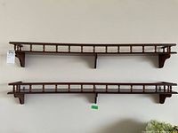 Front view of two wooden wall shelves with spindle rail detailing and support brackets, showing overall wear and scratches.
