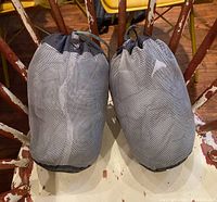 Two MEC sleeping bags stored in compact mesh carry sacks on a wooden chair.