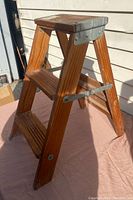 Full view of the wooden two-step hander stool with metal side supports and top metal brace.