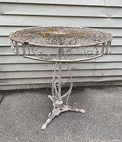 Full view of the wrought iron round garden table showing the intricate floral openwork tabletop and decorative edge band with leaf motifs.