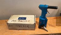 Blue pneumatic air riveter tool next to original box with handwritten 'AIR RIVETER' label