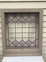 Front view of antique stained glass window panel with a geometric diamond pattern and textured purple glass within painted wooden frame.