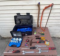 Wide view showing assortment of tools and open toolbox carrier on table with white siding background