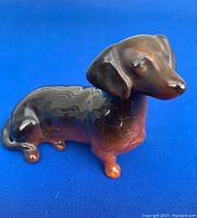 Front and side view of the ceramic dachshund figurine showing the brown and black gradient glaze and detailed facial features with ears and tail visible.