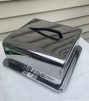 Full view of chromed steel cake carrier with lid and black handle, showing reflective surface and Art Deco lines.