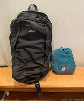 Front view of black Co-op backpack alongside blue MEC Mountain Equipment duffel in compact pouch on wooden surface