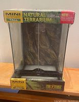 Front view of the terrarium in original packaging showing clear glass and printed background inside.