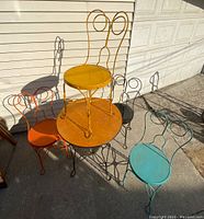 Photo showing the antique style ice cream parlour table with four different colored chairs stacked and arranged around it.
