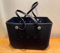 Side view of the large black Bogg beach tote bag showing its rectangular shape, perforations on sides, and two flexible handles.