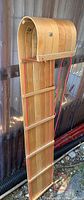 Full view of the maple wooden toboggan showing its length, curved front, horizontal wooden slats, and attached red rope for towing or steering.