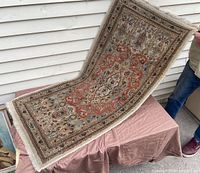 Full view of the Persian carpet being held to show entire length, colors and fringe edges visible.