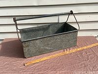 Full view of the rectangular galvanized metal tote with handle placed on a brown surface with a ruler beside it for scale.
