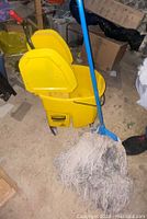 Side view of yellow Rubbermaid mop bucket with attached wringer and blue mop handle with mop head.