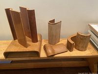 Wide shot showing all 7 plywood architectural samples on a wooden bench, featuring various curved shapes and teak veneer finish.