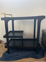 Side angle view of the black metal bar cart showing two lower shelves and open frame design.