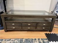 Front view of large dark wood coffee table with glass top and six metal-handled drawers visible