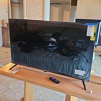 Front view of 43-inch Roku TV on wooden table with remote in front.