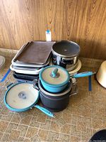 Overview of assorted cookware including stacked sheet pans, non-stick pots, Dutch ovens, and turquoise-handled saucepans.